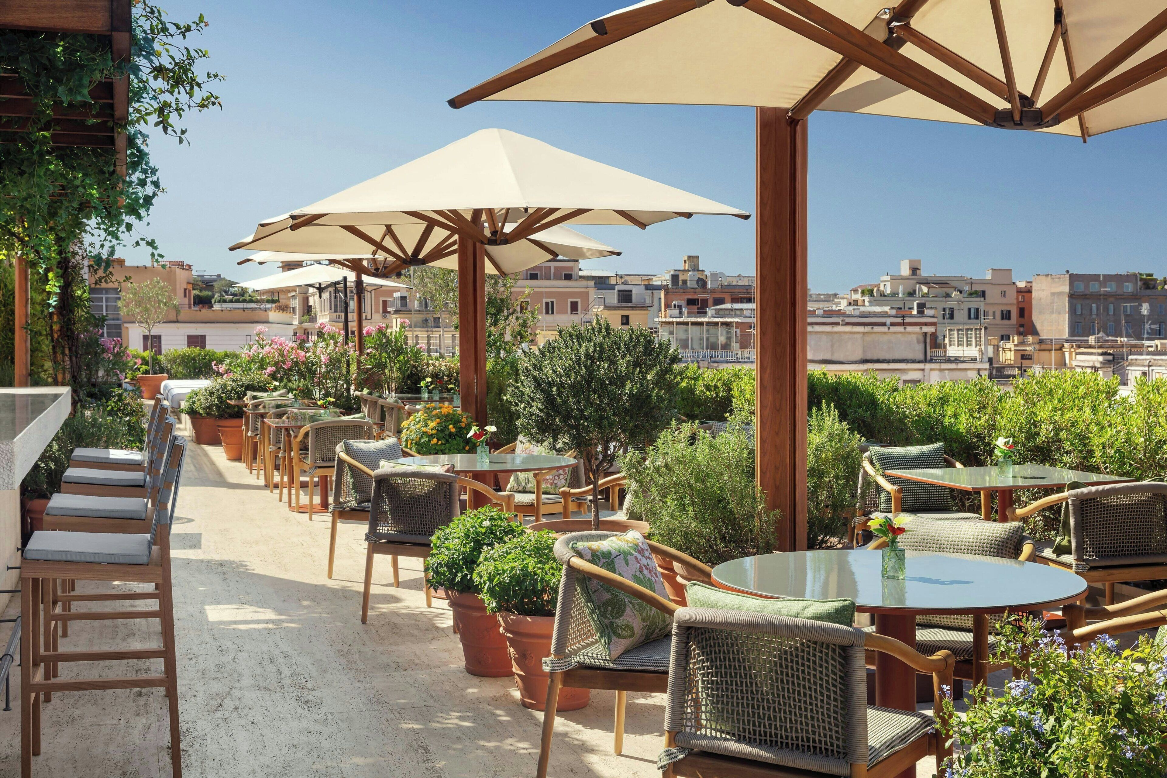 An outdoor patio with multiple tables and chairs, surrounded by potted plants and umbrellas.