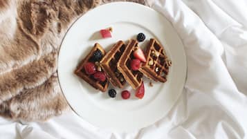 A plate of waffles with berries and nuts on a white plate, placed on a white bedspread.