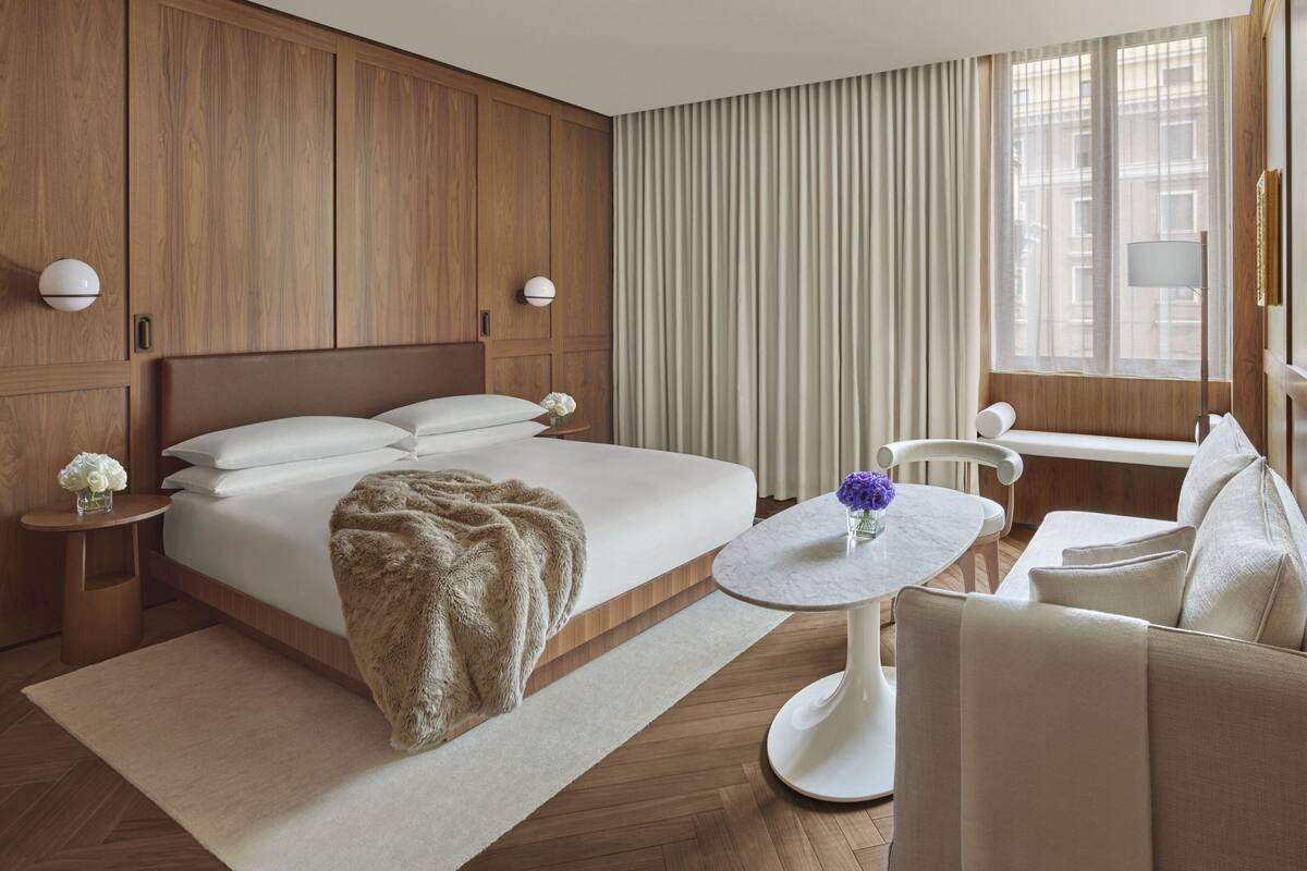 Habitació d'hotel amb un llit gran, una taula rodona, un sofà i una finestra amb cortines.