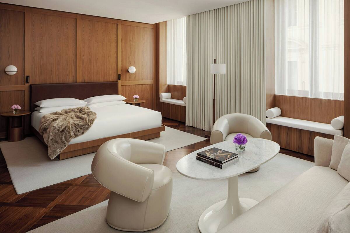 Habitació d'hotel moderna amb un llit gran, dues zones d'estar, una taula rodona i un gran finestral amb cortines.