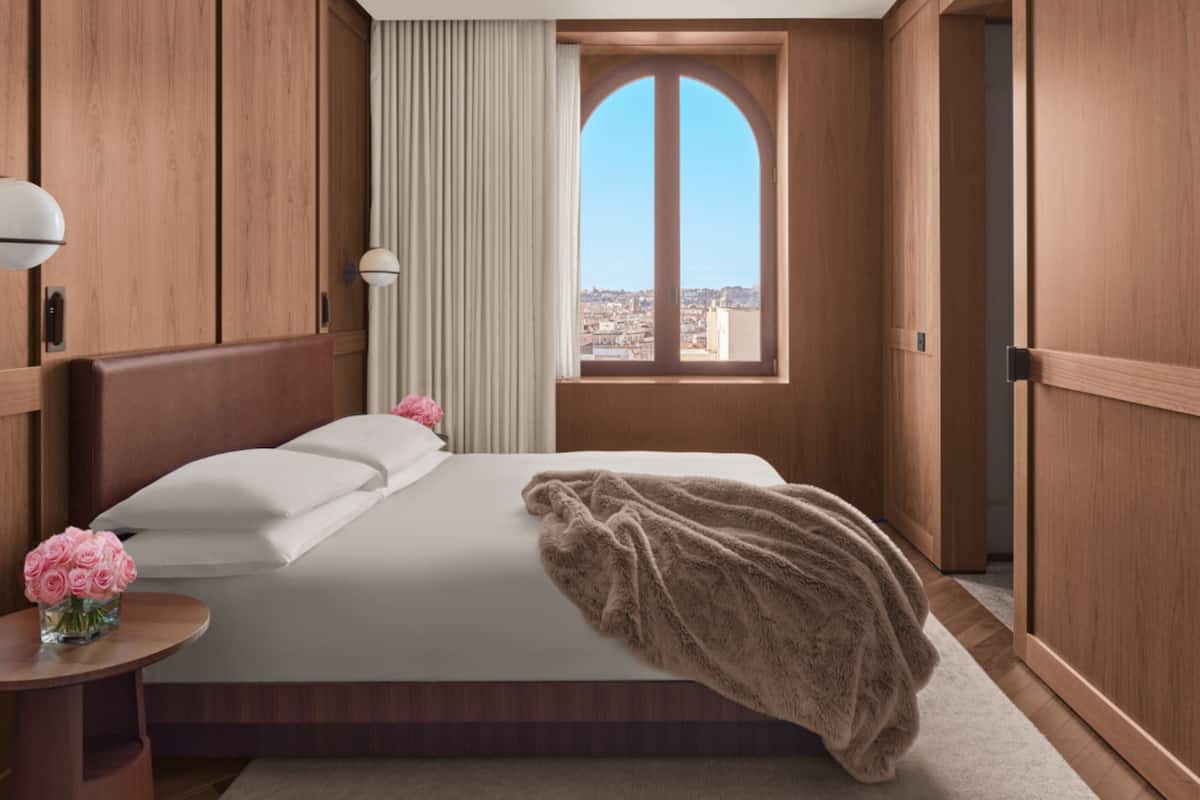 Habitació d'hotel amb llit, finestra que ofereix vistes, taulell de nit amb un ram de flors i panells de fusta.