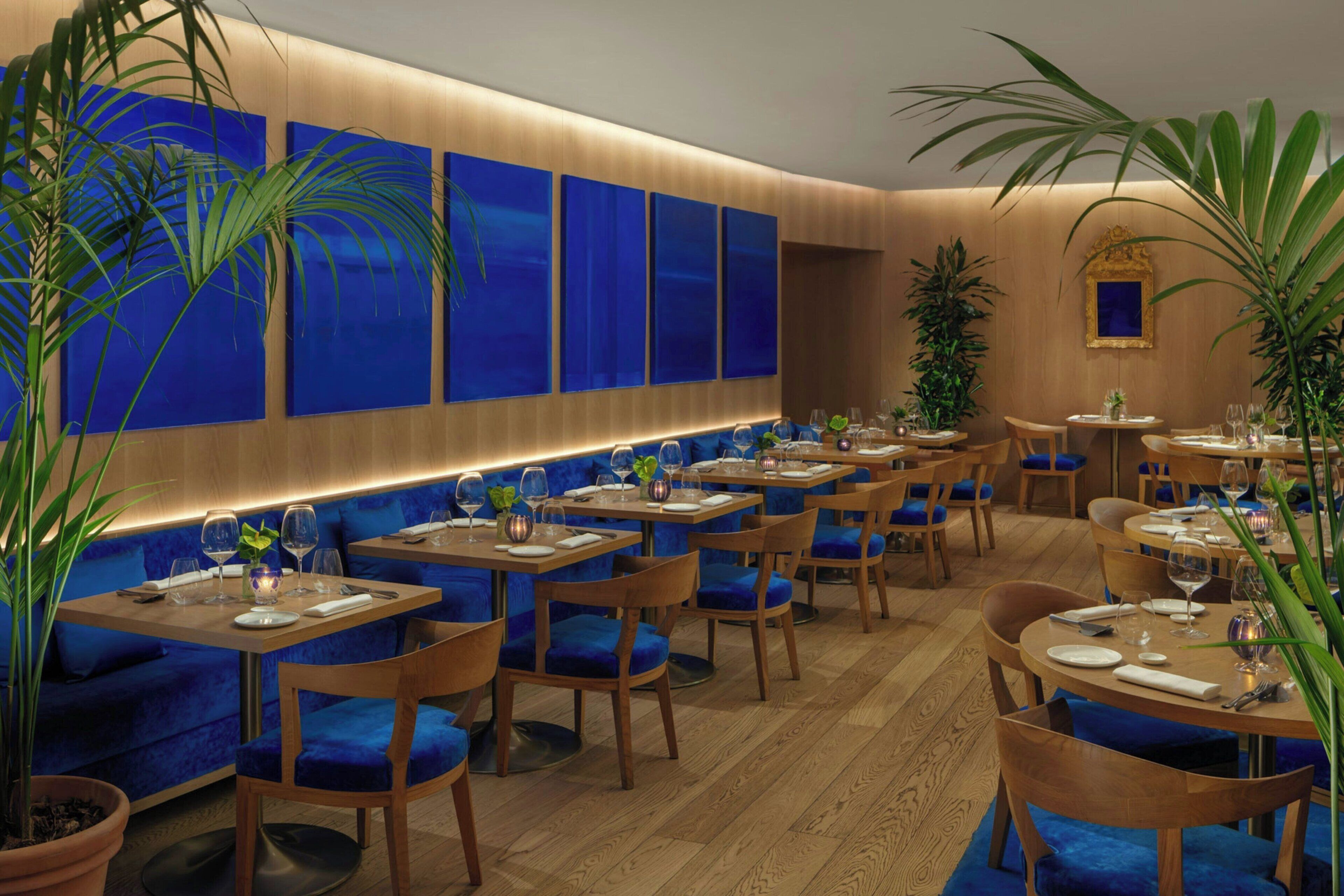 A restaurant with blue upholstered booths, wooden tables, and potted plants.