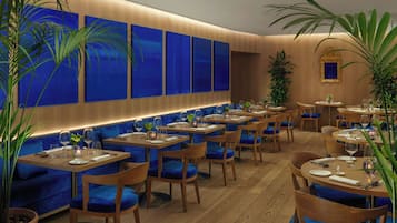 A restaurant with blue upholstered booths, wooden tables, and potted plants.