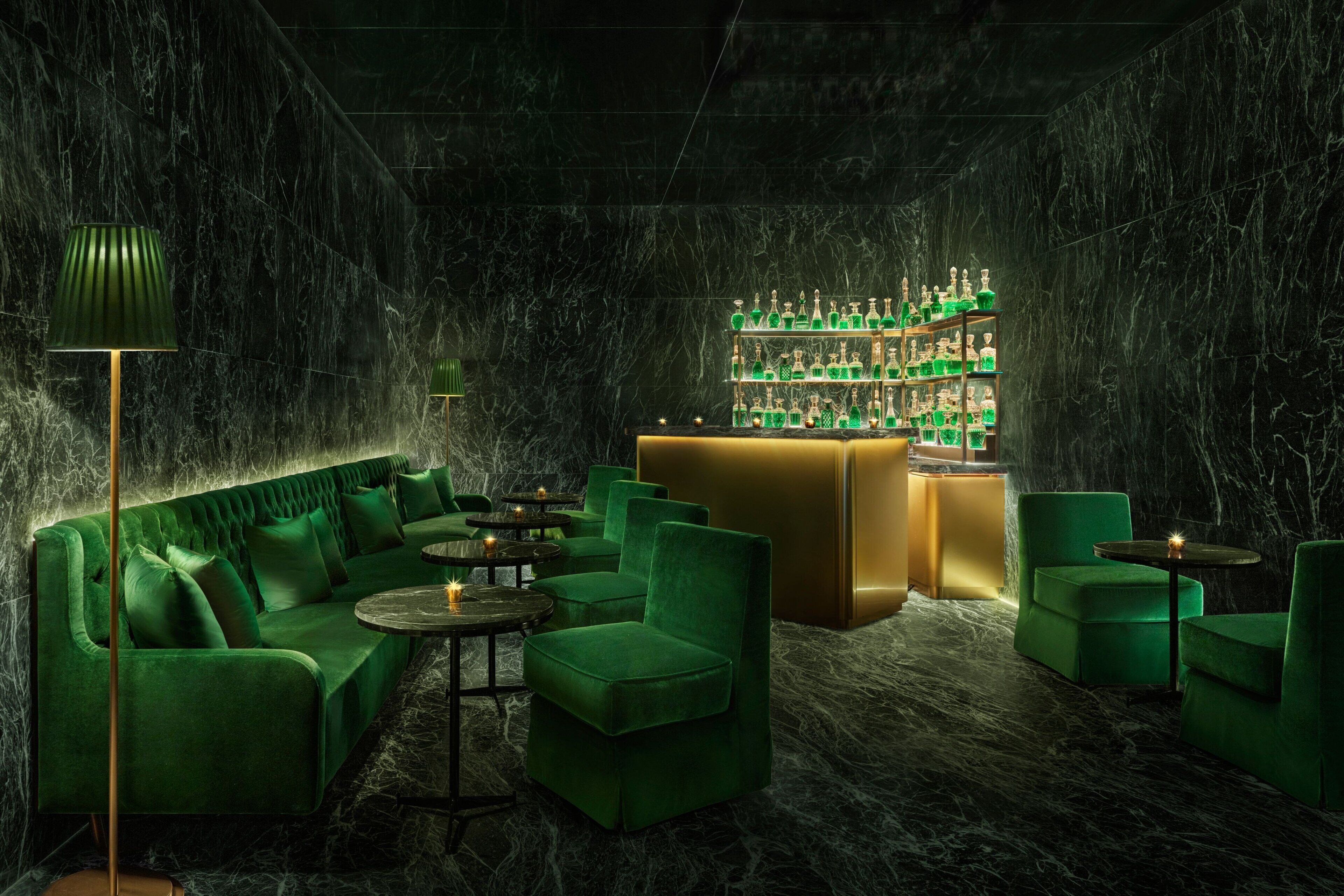 A luxurious green-themed bar area with marble walls, plush seating, and a well-stocked bar.
