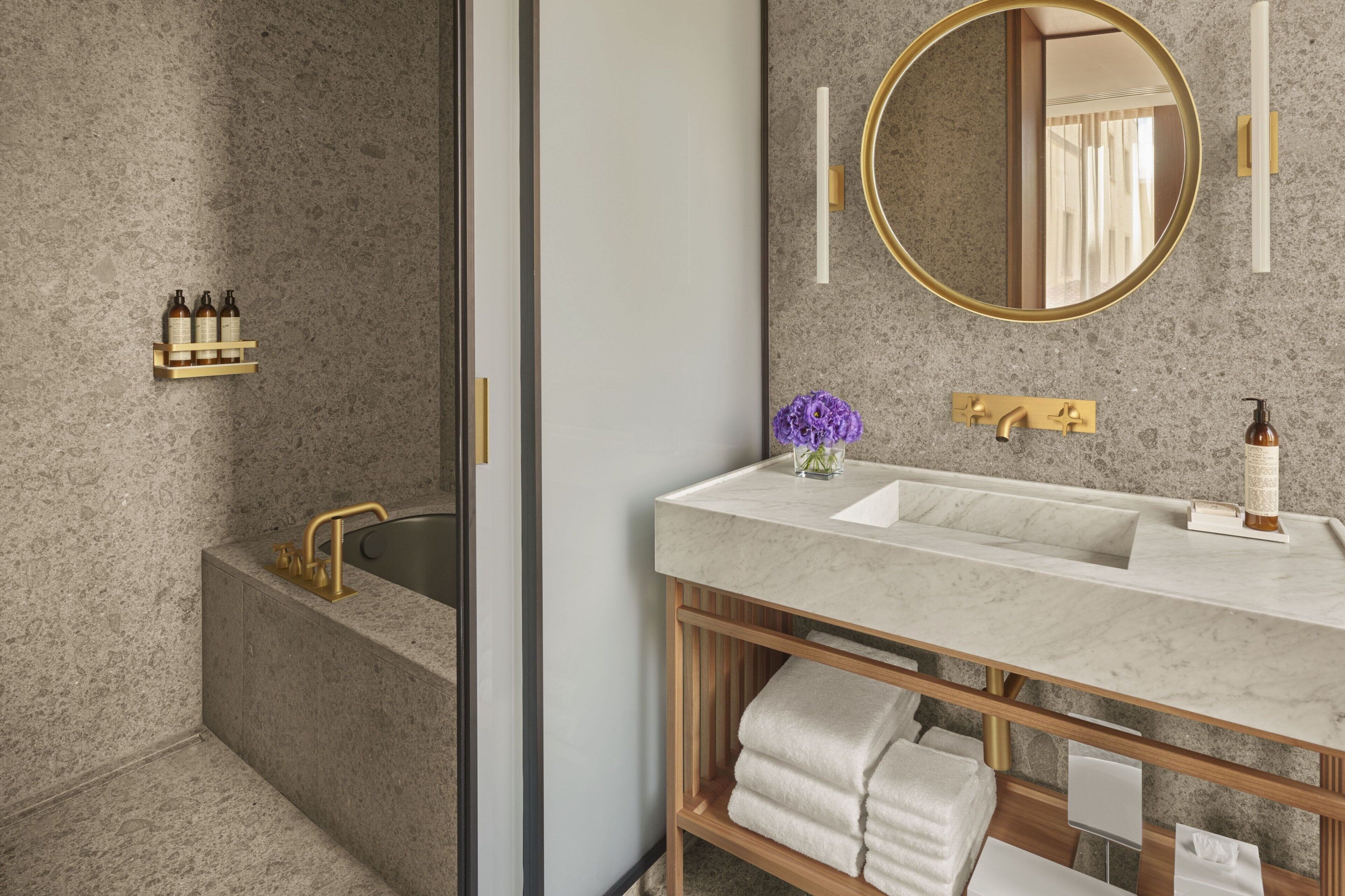 A modern bathroom with a freestanding bathtub, a vanity with a marble countertop, and a round mirror with a gold frame.