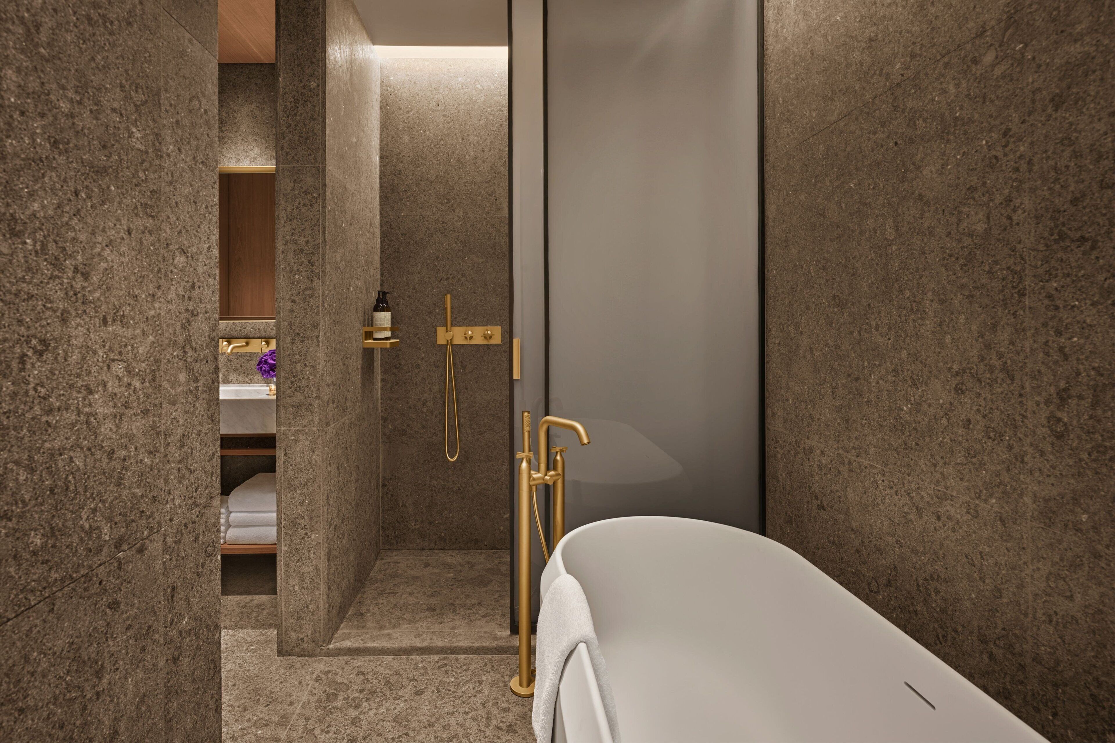 A modern bathroom with a freestanding bathtub, a shower area with gold fixtures, and a marble-tiled shower enclosure.
