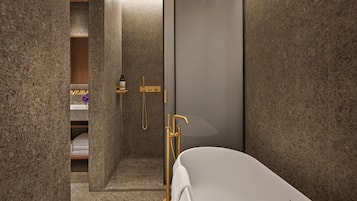 A modern bathroom with a freestanding bathtub, a shower area with gold fixtures, and a marble-tiled shower enclosure.