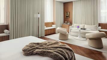 A modern hotel room with a large bed, two sofas, a coffee table, and a floor lamp.