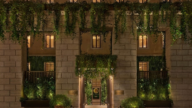 A building facade with a central entrance, flanked by two windows with curtains, and a balcony with greenery. - The Rome EDITION (Rome)