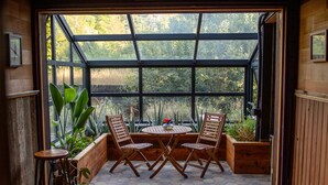 A sunlit patio with a wooden table and chairs, surrounded by planters and a large window offering a view of greenery. - The Gorge Onsen Spa (Washougal)
