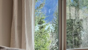 A bed with a white pillow and a view of a forest and mountains through a window. - The Gorge Onsen Spa (Washougal)