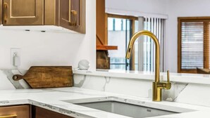 A kitchen with a white countertop, a gold faucet, and wooden cabinets. - Luxe DV Condo at Snow Park (Park City)