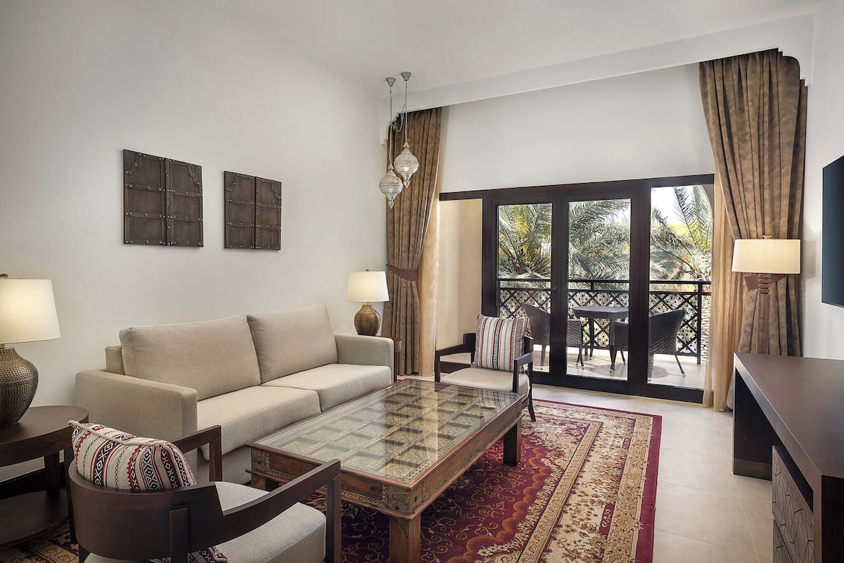A living room with a sofa, armchairs, a coffee table, and a view of an outdoor balcony.