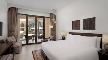 A hotel room with a large bed, a sofa, a desk, and a view of the outdoor area.