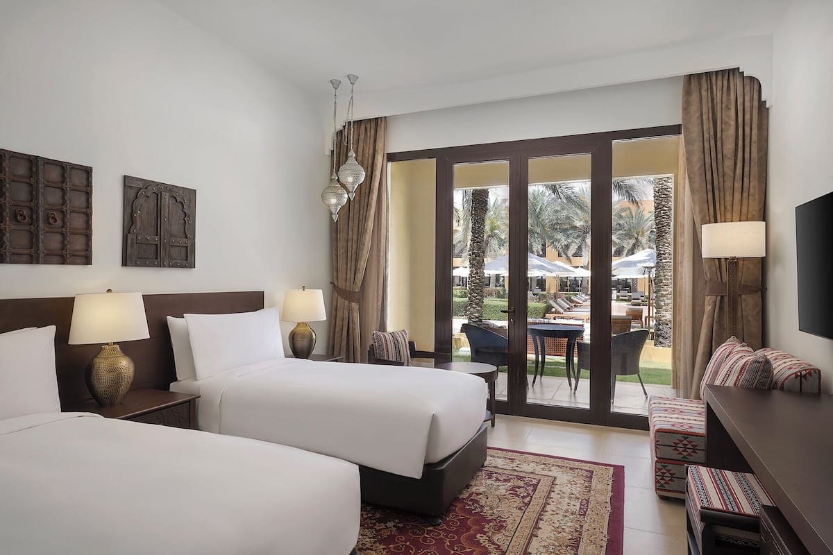 A hotel room with two beds, a sofa, a TV, and a balcony with outdoor seating.