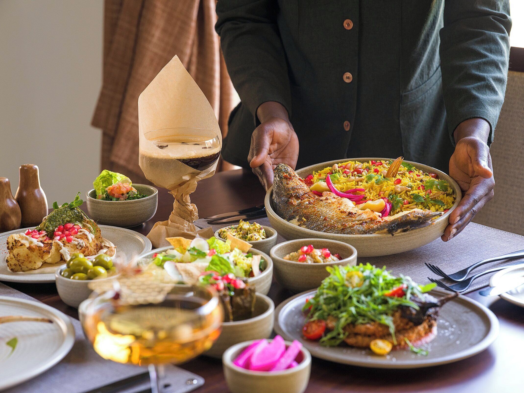 Diverse gerechten, waaronder een hele vis, rijst en salades, op een tafel.