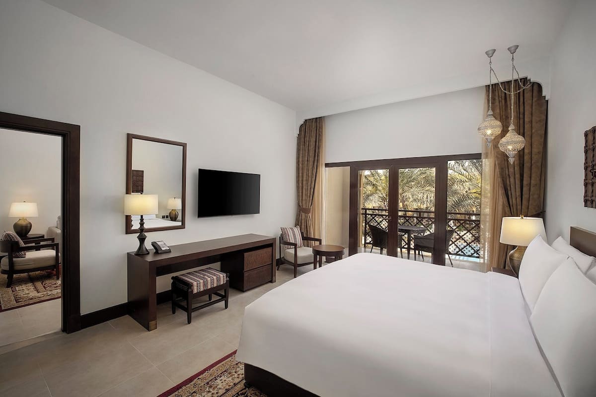 A hotel room with a large bed, a desk with a chair, a TV, and a balcony with a view.