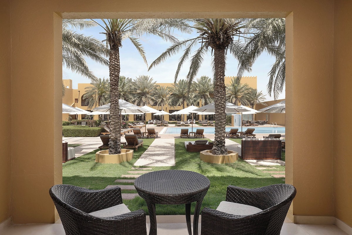 A view of a poolside area with lounge chairs, umbrellas, and palm trees.