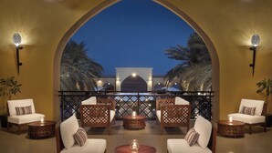 A balcony with a night sky view, furnished with white sofas and wooden tables, and palm trees in the background. - Aldhafra Resort, Vignette Collection by IHG (Madinat Zayed)