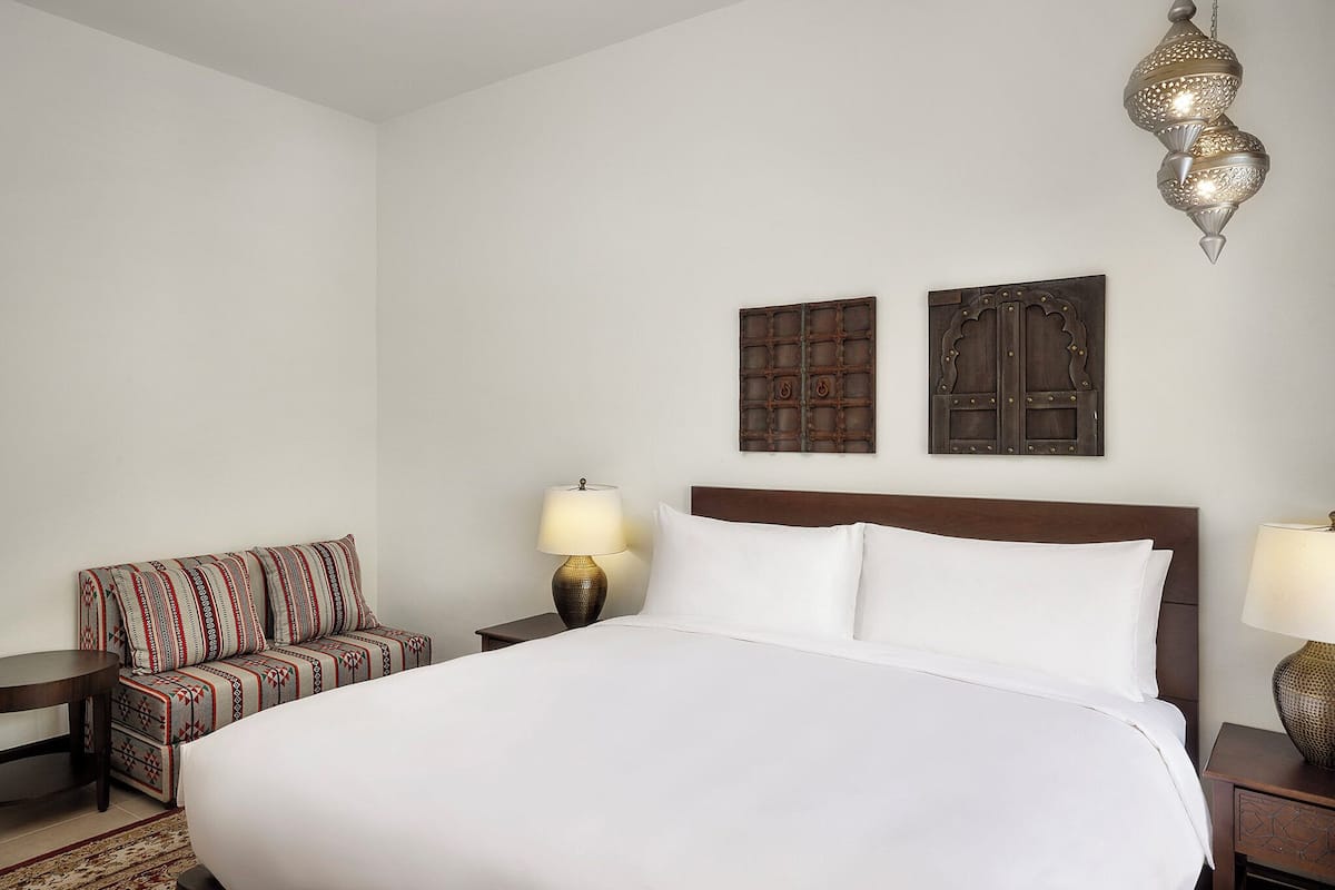 A hotel room with a large bed, a sofa, two wall-mounted lamps, and decorative wall art.