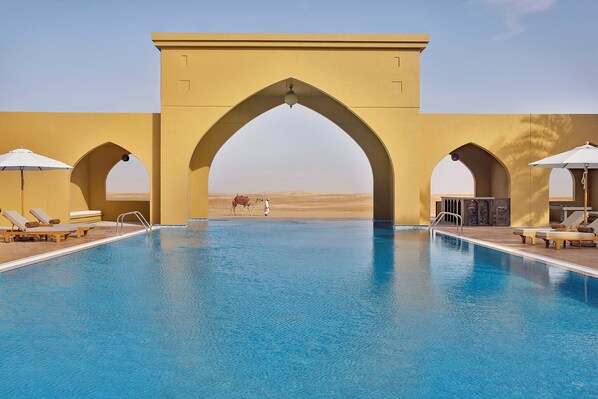 A swimming pool with a desert view, surrounded by arches and lounge chairs. - Aldhafra Resort, Vignette Collection by IHG (Madinat Zayed)