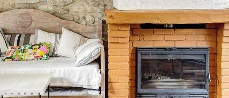 A rustic room with a stone wall, a wooden sofa, a fireplace, and a rooster painting.