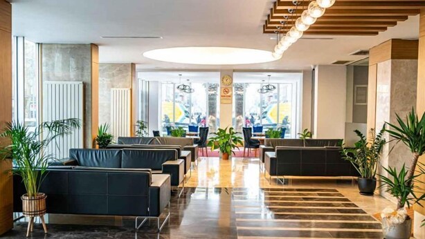 A modern hotel lobby with a central seating area, a staircase with hanging lights, and a view into the dining area. - HALLEY OTEL (Denizli)