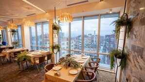 A modern dining area with large windows, wooden tables, and hanging plants. - HALLEY OTEL (Denizli)