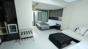 A modern hotel room with a bed, a sofa, a small table, a mini-fridge, and a bathroom visible through an open door. - HALLEY OTEL (Denizli)