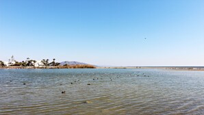 A calm lake with a clear sky, a distant mountain, and a few buildings on the shore.