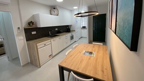 A modern kitchen with white cabinets, a wooden dining table, and a hanging light fixture.