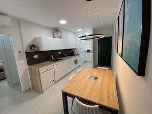 Une cuisine moderne avec des meubles blancs, une table à manger en bois et un luminaire suspendu.