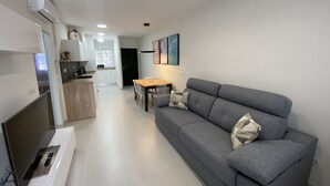 A modern living room with a grey sofa, a TV, and a dining area with a table and chairs.