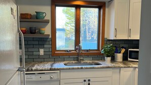 Una cocina moderna con armarios blancos, encimera de granito, lavavajillas integrado y una ventana sobre el fregadero.
