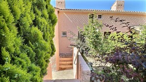 Un escalier en pierre mène à un bâtiment doté d’un toit en tuiles, qui est entouré d’une végétation luxuriante et agrémenté d’une plante en pot.