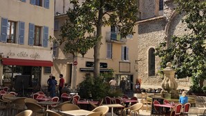 Un espace café en plein air avec des tables et des chaises, un bâtiment en pierre avec une fontaine et une enseigne indiquant « Les Cœurs Cafés ».