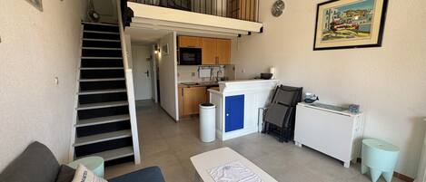 Un espace de vie compact comprenant un coin cuisine, un espace repas et un escalier menant à un niveau supérieur.