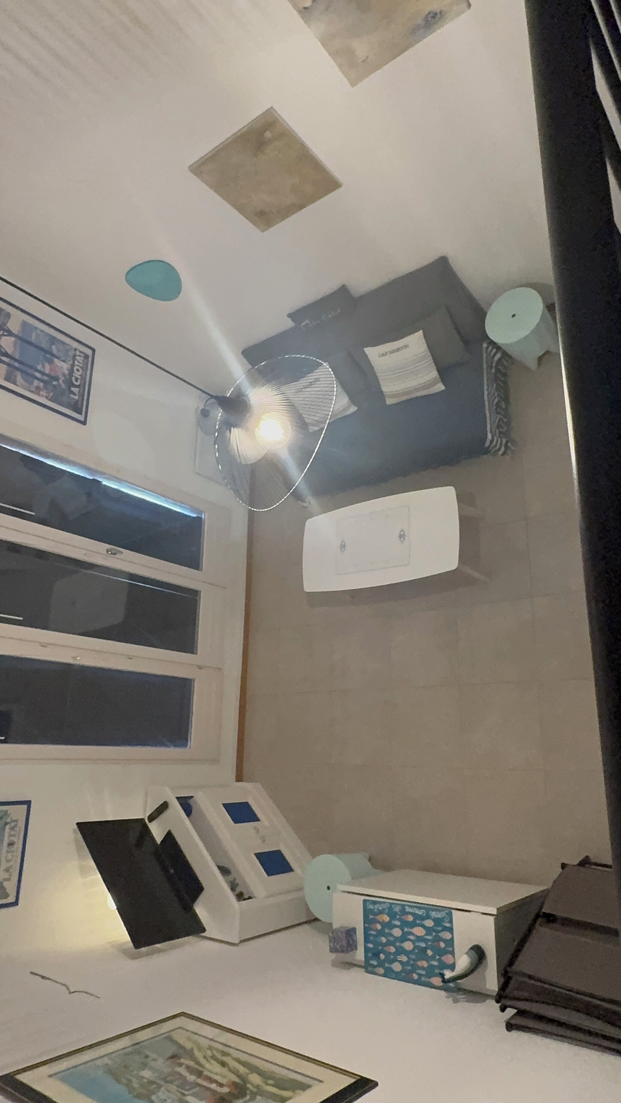A room with a ceiling fan, a mounted air conditioner, a window with blinds, and a framed picture on the wall.
