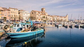 A marina with boats docked, a building with a tower, and a row of colorful buildings along the waterfront. - Duplex with sea view (La Ciotat)