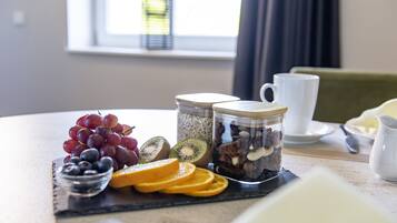 Una escena de desayuno con un bol de fruta, botes de nueces y semillas, y una taza sobre una mesa.