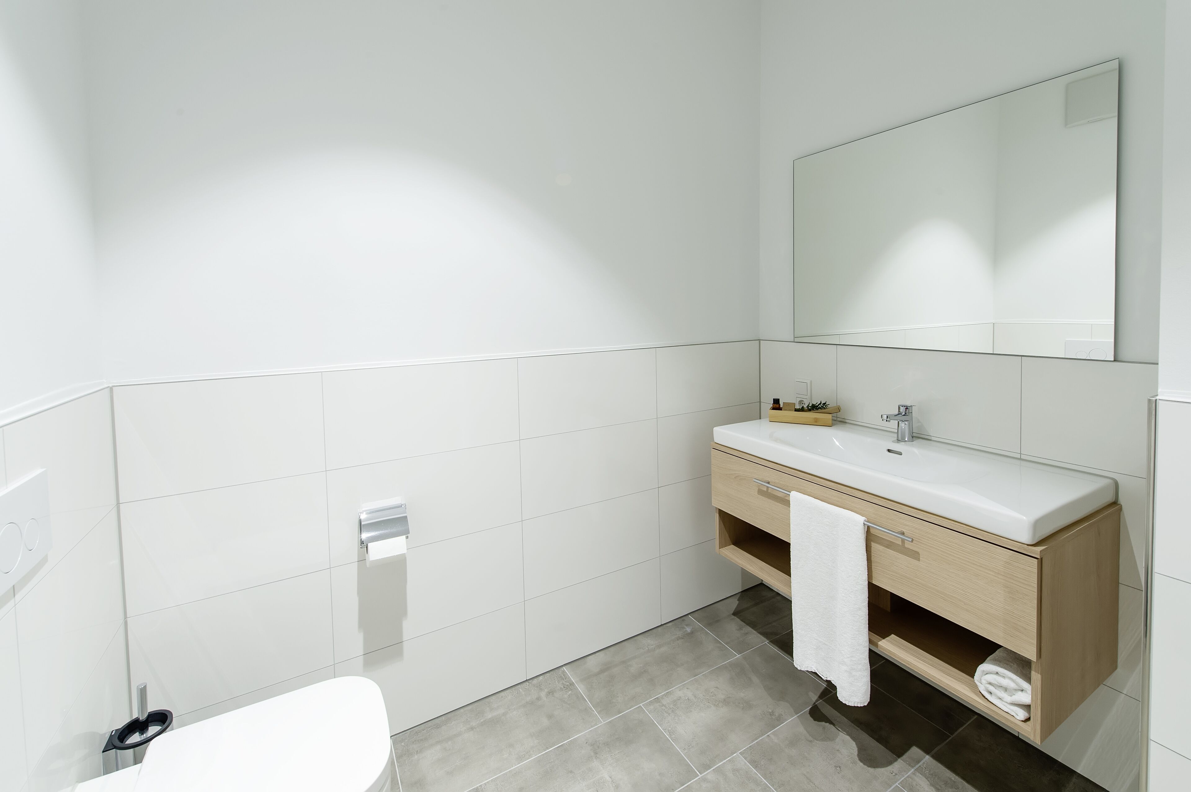 Un baño moderno con lavamanos blanco, espejo y suelo de baldosas grises.