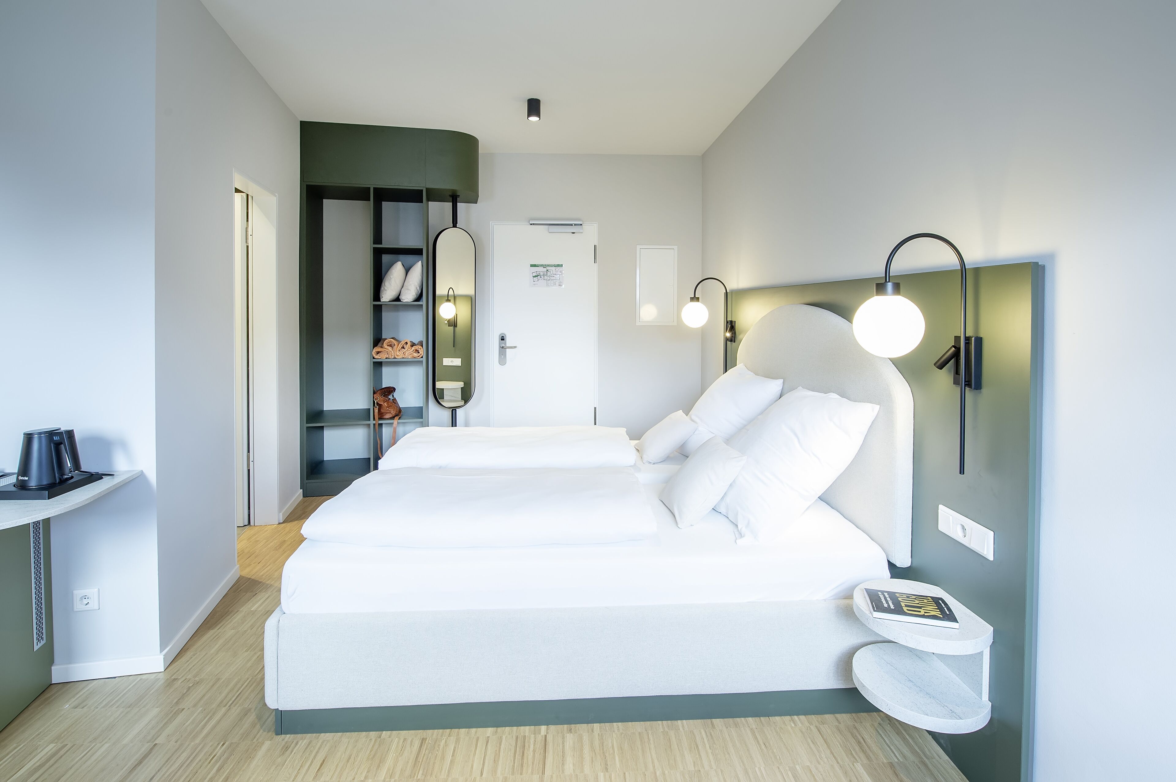 Una habitación de hotel moderna con una cama grande, mesitas de noche, un armario y una pequeña zona de estar.