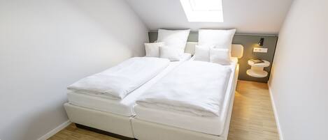 Un dormitorio moderno y luminoso con tragaluz, una cama con ropa de cama blanca, una mesita de noche y una lámpara de noche pequeña.