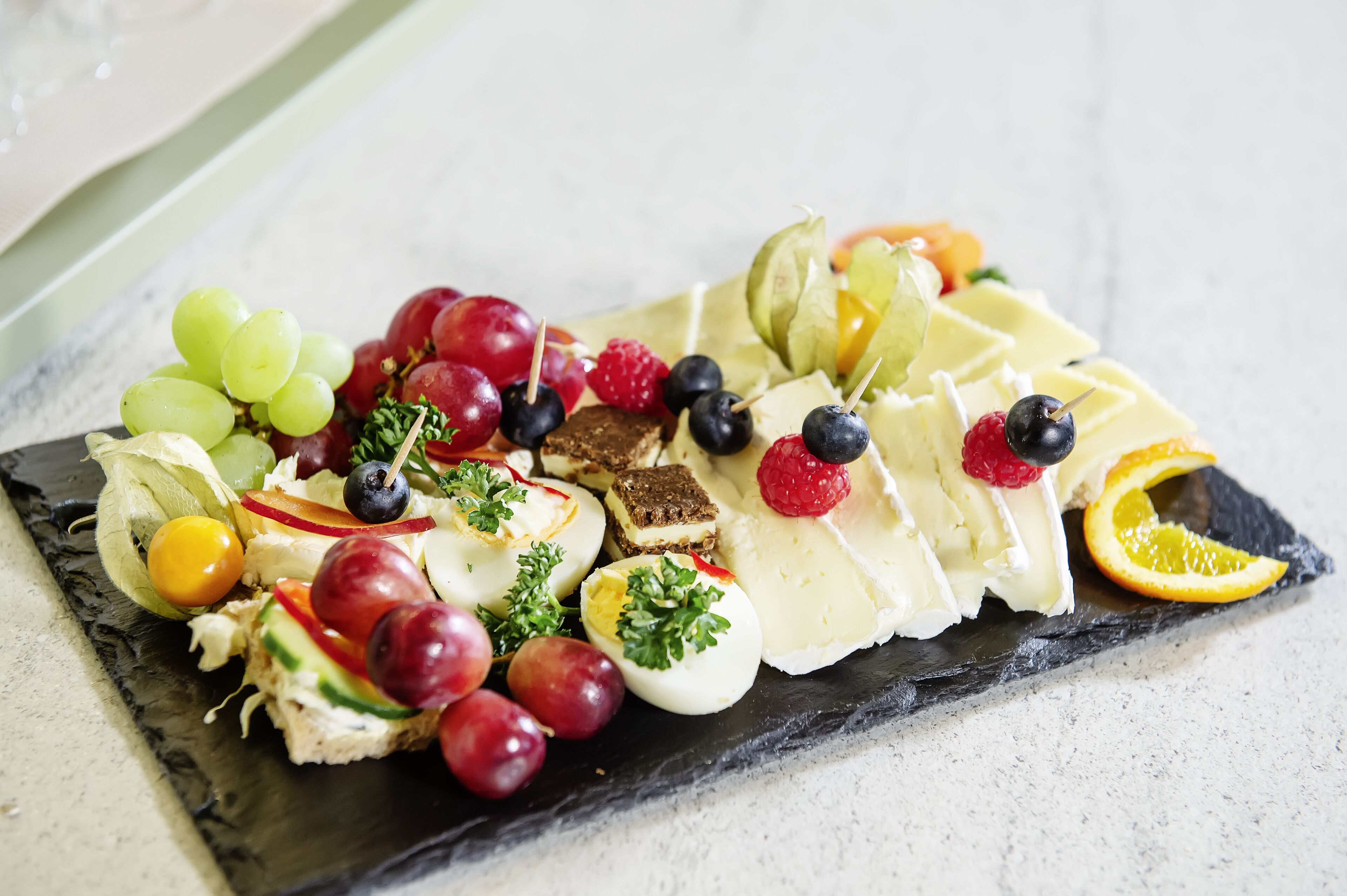 Een charcuterieplank met diverse kazen, fruit en noten op een leistenen plank.