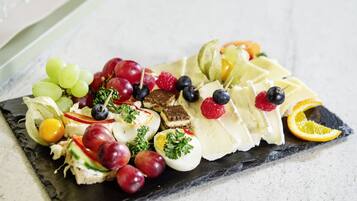 Een charcuterieplank met diverse kazen, fruit en noten op een leistenen plank.