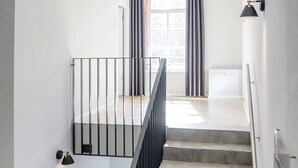 Una escalera con base de ladrillo y baldosas grises, que conduce a una plataforma con barandilla negra y una ventana con cortinas.