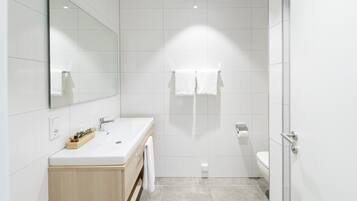 Een moderne badkamer met een grote spiegel, een houten wastafelmeubel, een douchegedeelte en een toilet.