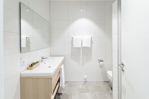 Un baño moderno con un espejo grande, un tocador de madera, zona de ducha y un inodoro.