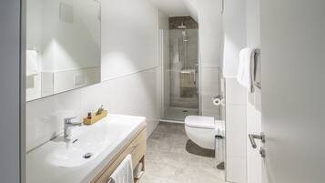 A modern bathroom with a large mirror, a white sink, a shower enclosure, and a toilet.