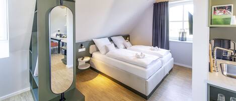 A modern bedroom with a large bed, a bedside table, a mirror, and a window with curtains.